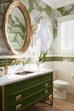 a bathroom with green and white wallpaper, gold accents and a round mirror above the sink