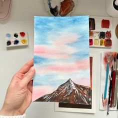 a person holding up a piece of paper with watercolors and paint on it