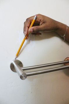 a person holding a pencil in their left hand while standing next to a toilet paper dispenser