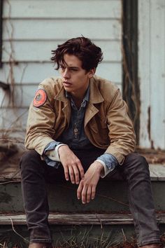 a young man sitting on top of a wooden bench next to a building and looking off into the distance