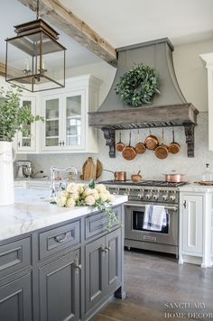 a kitchen with gray cabinets and white counter tops, an oven hood over the stove