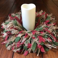 a white candle sitting on top of a wooden floor next to a red and green wreath