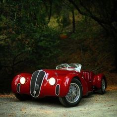 a red sports car parked on the side of a road in front of some trees