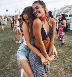 two young women hugging each other in the middle of a field at a music festival