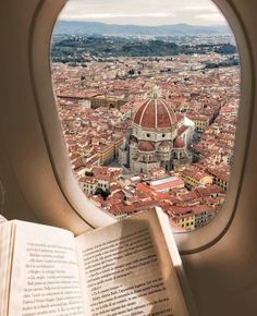 an open book sitting on top of a window sill next to a view of a city