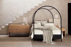 a bed with white sheets and pillows under a black iron frame in a neutral bedroom