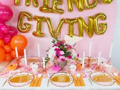 the table is set with pink and orange balloons, plates, cups, and utensils