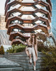 a woman sitting on the steps in front of a building with an unusual structure behind her