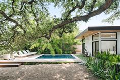 a pool in the middle of a yard next to a tree and some chairs on the ground