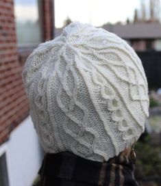 a person wearing a white knitted hat looking out at the street in front of a brick building