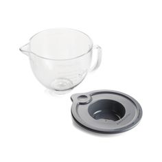 a glass measuring cup with a plastic lid next to a bowl on a white surface