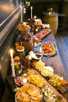 a long table filled with lots of food on top of a wooden table next to candles