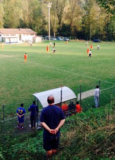 a group of people standing on top of a lush green field next to a soccer field