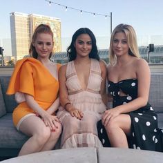 three women sitting on a couch in front of a cityscape with lights strung above them