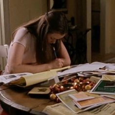 a woman sitting at a table with papers and pens in her hand, writing on a piece of paper