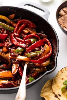 a skillet filled with peppers and tortillas next to some pita chips