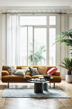 a living room filled with furniture next to a large window and potted palm tree