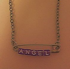 a necklace with the word angel on it hanging from a chain that is attached to a wall