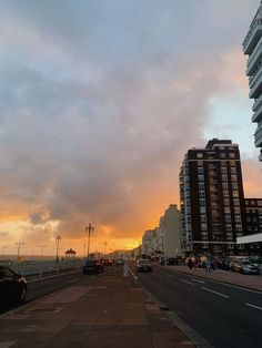 cars are parked on the side of the road near tall buildings and water at sunset