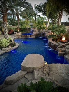 an outdoor pool surrounded by palm trees and water features a fire pit in the middle