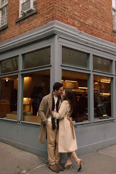 a man and woman standing in front of a store window with their arms around each other