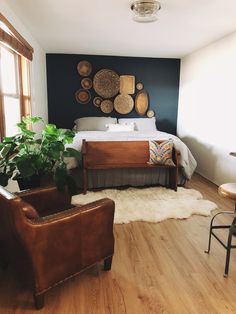 a bed room with a neatly made bed next to two chairs and a plant in the corner