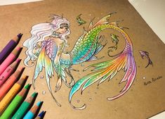 colored pencils are next to a drawing of a mermaid with long hair and fish tails