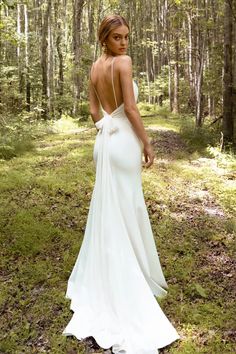 a woman standing in the woods wearing a white dress with a bow on it's back