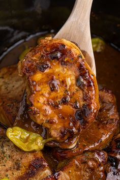 a wooden spoon in a slow cooker filled with meat and vegetables that are cooked