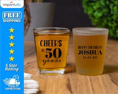 two shot glasses with cheers to 50 years printed on the front and back, sitting on a table next to each other