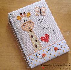 a cross stitch book with a giraffe and heart on the cover, sitting on a wooden surface