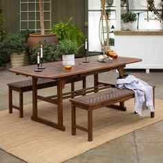 a wooden table with two benches next to it on a rug in front of potted plants