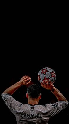 a man holding a soccer ball up to his head in front of a black background