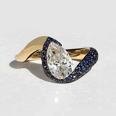 an oval shaped diamond ring with blue and white diamonds on the band, set in yellow gold