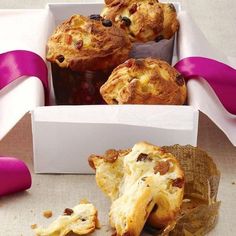 three muffins in a white box with pink ribbon around them and one has been eaten