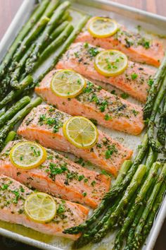 salmon and asparagus on a baking sheet with lemons, parsley and seasoning