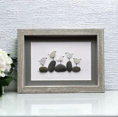 three little birds sitting on rocks in a shadow frame next to white flowers and pebbles