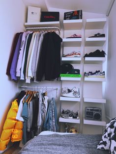 a closet with clothes hanging on the wall and shelves above it, next to a bed