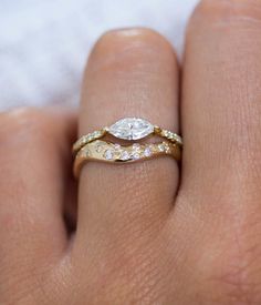 a woman's hand with two wedding rings on top of her finger and the ring has an oval shaped diamond