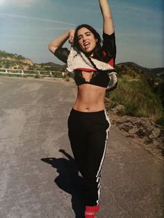 a woman in black and white outfit standing on the side of a road with her arms up