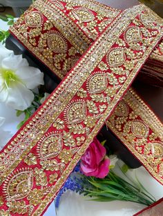 two pieces of red and gold ribbon on top of each other with flowers in the background