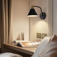 a desk with a lamp on it next to a book and some pillows in a room