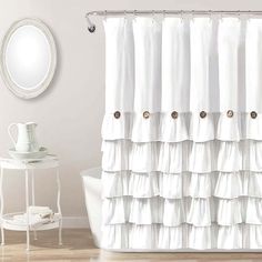 a white shower curtain with ruffles on the bottom and a mirror above it