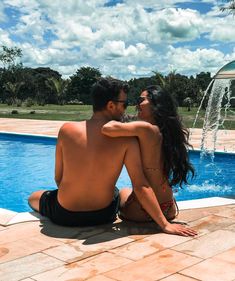 a man and woman sitting next to a swimming pool with a fountain in the background