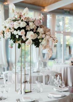 a tall vase filled with white and pink flowers on top of a dining room table