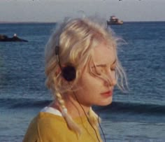 a woman with blonde hair wearing a yellow shirt and headphones in front of the ocean