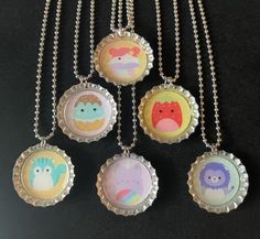 six bottle caps with different designs on them hanging from a silver ball chain that is attached to a black surface