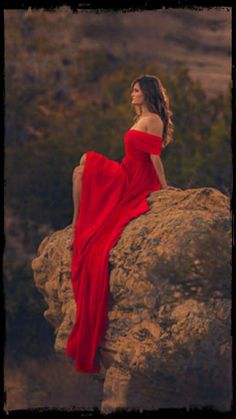 a woman in a red dress sitting on top of a rock