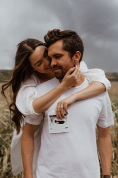 a man and woman embracing in the middle of a wheat field with storm clouds overhead