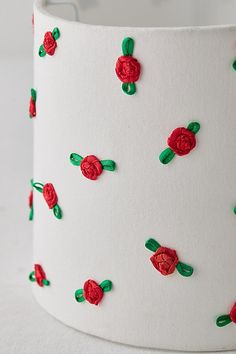 a white lamp shade with red roses on it and green stems in the middle, sitting on a table